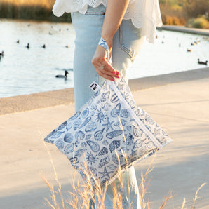 A woman stands on a concrete path by a pond with ducks, holding a Roamio by Bumkins Wet Bag: Shells.