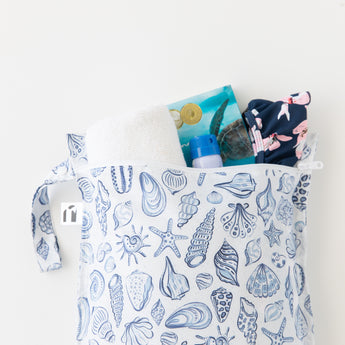 Roamio by Bumkins Wet Bag: Shells holds a towel, swimsuit, sunscreen, and book on a white background.
