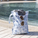 A bag from Roamio by Bumkins The Commuter Essential 4-Piece Set: Shells holds a water bottle, towel, & sunglasses poolside.