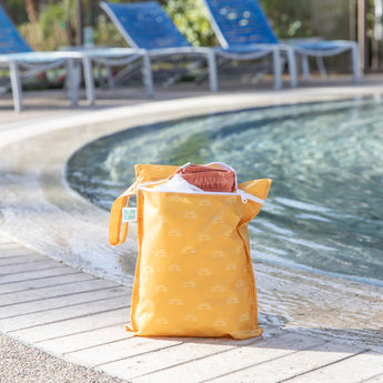 Bumkins Wet Bag: Sunshine holds clothes poolside with empty blue lounge chairs in the background.