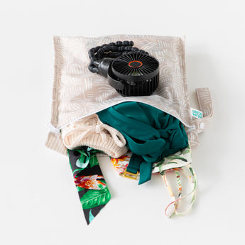 Bumkins Wet Bag: Wander lays open on a white background with swimsuit & clothes inside; a black fan lays on top.