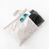 A bag from Bumkins Wet Bag + Wet/Dry Bag Set: Wander holds shoes, a towel, a book, and sunglasses on a white background.