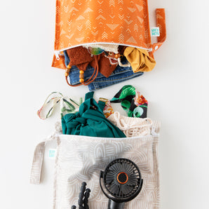Bumkins Wet Bag 2 Pack: Wander + Grounded holds clothes, swim wear, and a black fan on a white background.