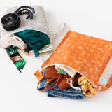 Bumkins Wet Bag 2 Pack: Wander + Grounded lays open on a white background with swimwear and clothes peeking out and a black fan.