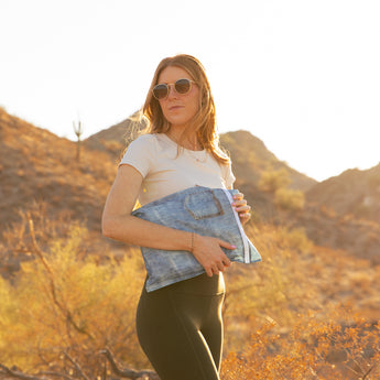 A woman in sunglasses holds a bag from Roamio by Bumkins The Commuter Deluxe 5-Piece Set: Denim On Denim in golden sunlight.