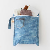 A bag from Roamio by Bumkins The Commuter Essential 4-Piece Set: Denim on Denim holds clothes & more on a white background.