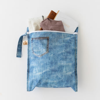 A bag from Roamio by Bumkins The Commuter Essential 4-Piece Set: Denim on Denim holds clothes & more on a white background.