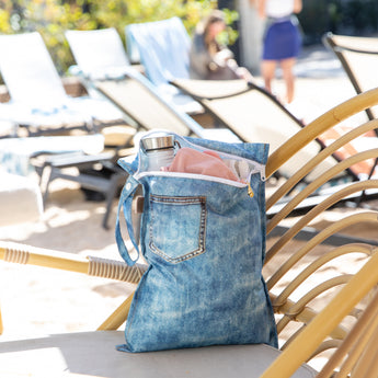 A bag from Roamio by Bumkins The Commuter Essential 4-Piece Set: Denim on Denim on a rattan chair with clothes & a bottle inside.
