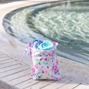 A Bumkins Wet Bag + Wet/Dry Bag Set: Watercolor with a blue towel holds pool essentials by the edge of the swimming pool.