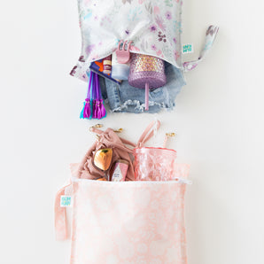 Bumkins Wet Bag 2 Pack: Floral and Lace holds a swimsuit, clothes, water bottles, sunglasses, and toiletries on a white background.