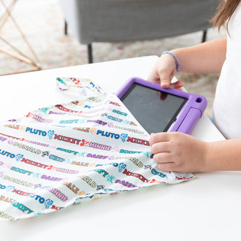 A child places a tablet in a bag from Bumkins On-The-Go Mealtime 7-Piece Set: Mickey & Friends MVP on a white table.