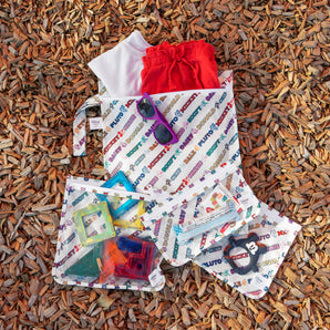 Bumkins The Chaos Coordinator Essential 4-Piece Set: Disney Mickey & Friends Varsity lays on brown wood chips with toys and clothes inside.