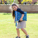 A girl smiles, holding a bag from Bumkins Wet Bag + Wet/Dry Bag Set: Mickey & Friends Forever outdoors on a grassy field.