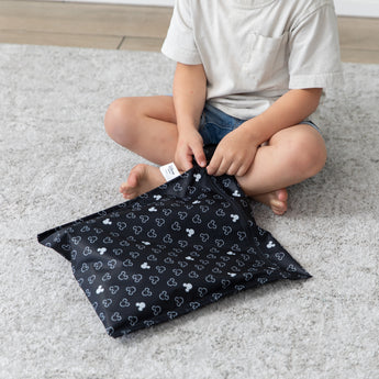 A boy unzips a Bumkins Wet Bag: Mickey Mouse Icon Black + White while sitting on a gray rug.