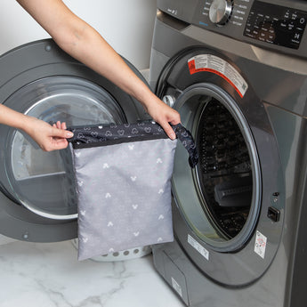 A person holds a bag from Bumkins The Chaos Coordinator Essential 4-Piece Set: Mickey Mouse Icon Black + White in front of an open washer.