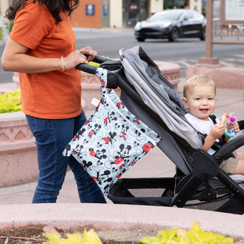 A person in jeans pushing a stroller outside with a Bumkins Wet Bag: Mickey & Friends Forever attached to the handle.