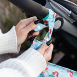 Hands with black nails attach a Bumkins Wet Bag: Disney Princess Ariel to a stroller handle using the snap closure of the strap.