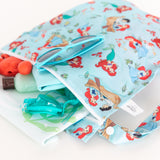Close-up of Bumkins Wet Bag: Disney Princess Ariel on a white background, filled with goggles, sunglasses, and swimwear.