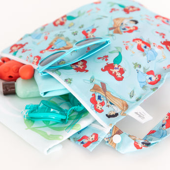 Close-up of Bumkins Wet Bag: Disney Princess Ariel on a white background, filled with goggles, sunglasses, and swimwear.