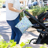 A person outdoors with a stroller, featuring a Bumkins Wet Bag: Aloha Stitch for attached to the handle.