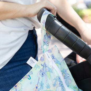 Close-up of a person pushing a stroller with a Bumkins Wet Bag: Aloha Stitch hanging from the handle.