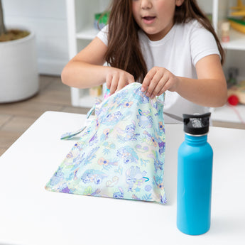 A child opens the Bumkins Wet Bag: Aloha Stitch at a table next to a blue water bottle, highlighting its reusable features.