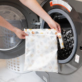 A person holds a bag from Bumkins The Chaos Coordinator Essential 4-Piece Set: Disney Winnie + Friends in front of an open washing machine.