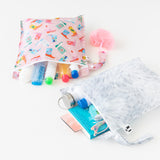 Roamio by Bumkins Wet Bag 2 Pack: Disco Boots lays open on a white background with toiletries, a book, glasses, & water bottle peeking out.