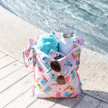 A Roamio by Bumkins Wet Bag 2 Pack: Disco Boots with summer essentials sits poolside on a sunny day.