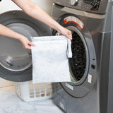 A person holds a Roamio by Bumkins Wet Bag 2 Pack: Disco Boots in front of an open front-loading washing machine.