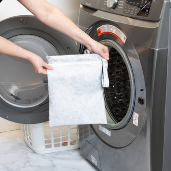 A person holds a Roamio by Bumkins Wet Bag 2 Pack: Disco Boots in front of an open front-loading washing machine.