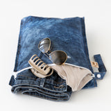 A Roamio by Bumkins Wet Bag 2 Pack: Denim On Denim rests open on a white background with clothes, sunglasses, & hair clip inside.