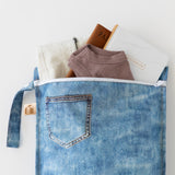 The Roamio by Bumkins Wet Bag 2 Pack: Denim On Denim holds a notebook, brown shirt, pants & passport on a white background.