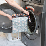 A person holds a Bumkins Wet Bag 2 Pack: Everyday Is Halloween in front of an open front-loading washing machine.