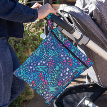 A person pushes a stroller outdoors with a Bumkins Wet Bag 2 Pack: Jungle + Animal Prints attached to the handle.