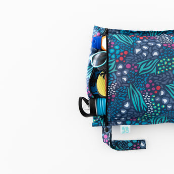 A Bumkins Wet Bag 2 Pack: Jungle + Animal Prints is partially visible on a white background, filled with a water bottle, shoes, and sunglasses.