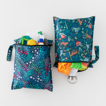 Bumkins Wet Bag 2 Pack: Jungle + Animal Prints sits side by side on a white background, filled with beach essentials like sand toys and swimwear.