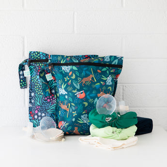 Bumkins Wet Bag 2 Pack: Jungle + Animal Prints sits against a white brick wall with cloth diapers and breast pump parts on a white counter.