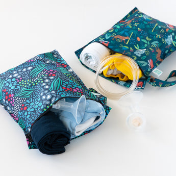 Bumkins Wet Bag 2 Pack: Jungle + Animal Prints filled with folded clothes, cloth diapers, and breast pump parts on a white background.