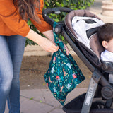 A person zips a Bumkins Wet Bag 2 Pack: Jungle + Animal Prints attached to a stroller outdoors with a child inside.