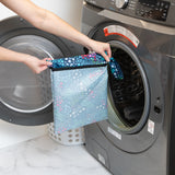 A person holds a Bumkins Wet Bag 2 Pack: Jungle + Animal Prints in front of an open washing machine.