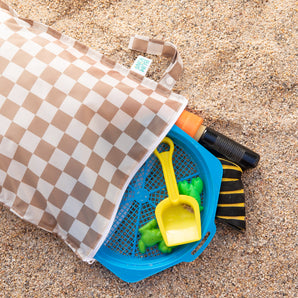 A Bumkins Wet Bag Plus 2 Pack: Mauve + Sand Check lays open on sand with beach toys spilling out.