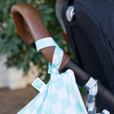Close-up of a Bumkins Wet Bag Plus 2 Pack: Mint + Charcoal Check hanging from a stroller handle outdoors.