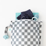 A Bumkins Wet Bag Plus 2 Pack: Mint + Charcoal Check holds baby items like a book, pants, teether, and pacifier on a white background.