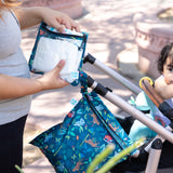 A person packs baby essentials in bags from Bumkins The Chaos Coordinator Essential 4-Piece Set: Jungle by a stroller with a baby outdoors.