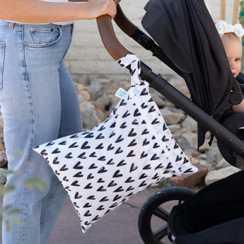A person pushes a stroller with a Bumkins Wet/Dry Bag Set: Hearts, featuring black hearts, attached to the handle.