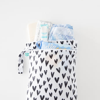The Bumkins Wet Bag + Wet/Dry Bag Set: Hearts holds diapers, cream, and a book on a white surface.