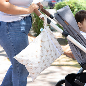 A child sits in a stroller while a Bumkins Palm Daze Wet Bag hangs from the handle.