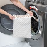 A person holds Bumkins Wet/Dry Bag: Sand Check in front of an open front-loading washing machine.