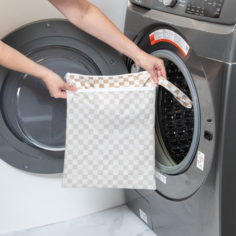 A person holds a bag from Bumkins Wet Bag + Wet/Dry Bag Set: Sand Check in front of an open front-loading washing machine.